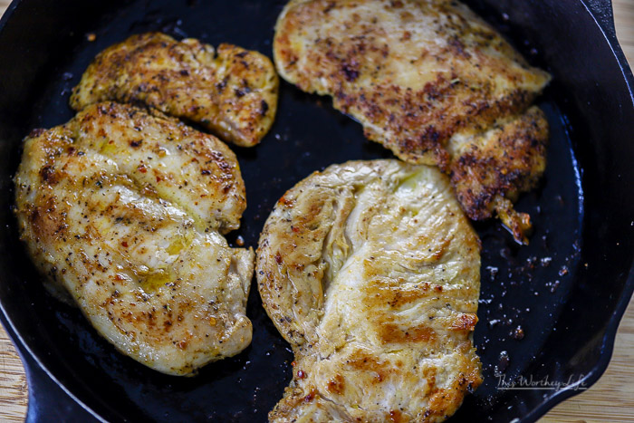 chicken breasts cooking in a cast iron skillet