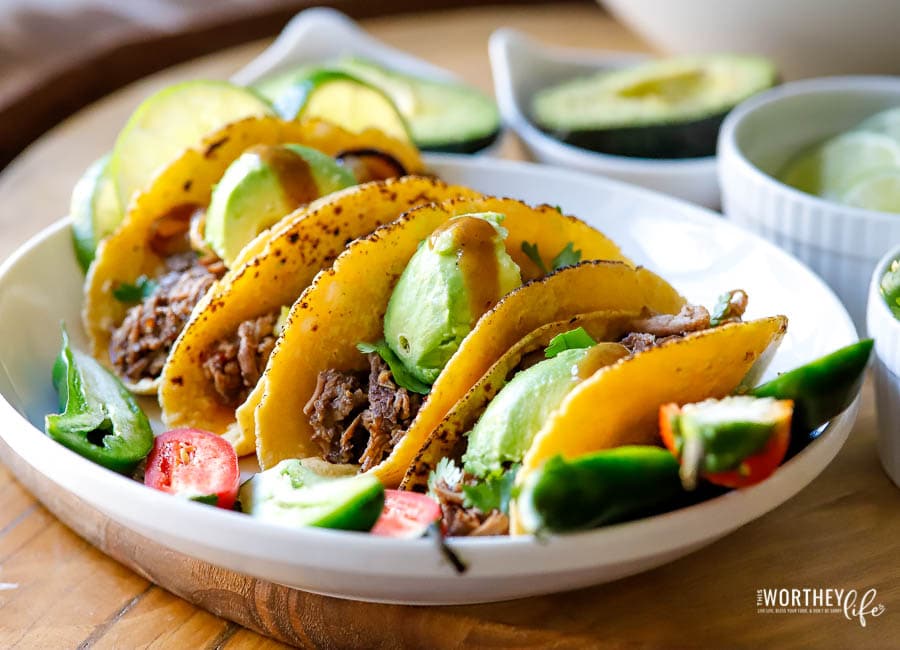  beef tacos on a white plate with limes