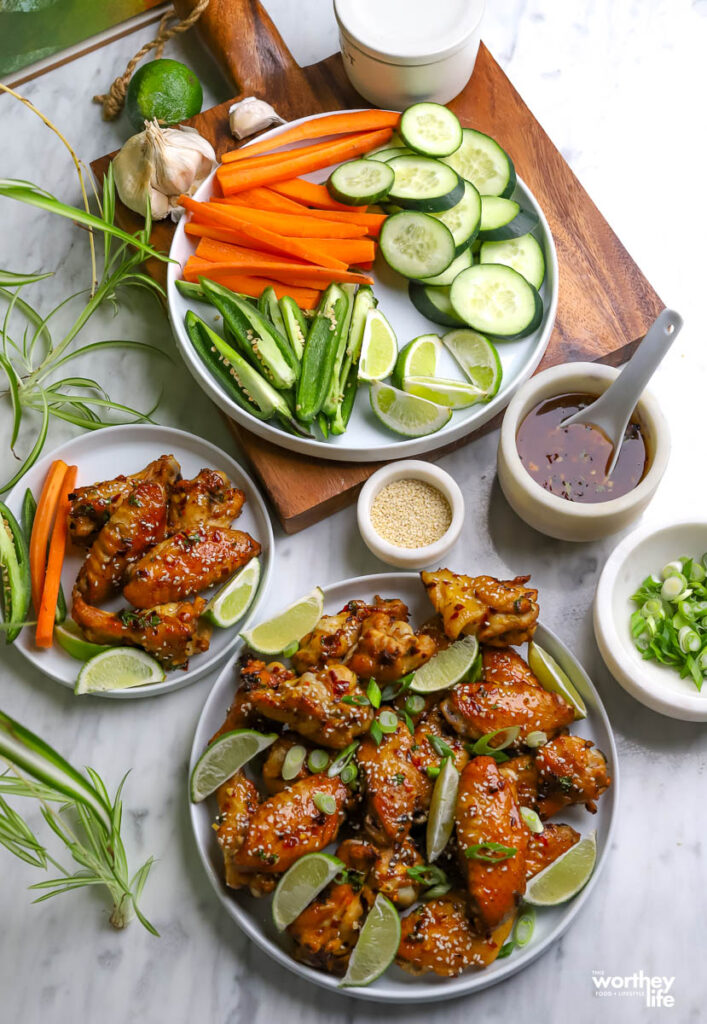 A spread of Thai chicken wings served with a sauce and lots for fresh vegetables.