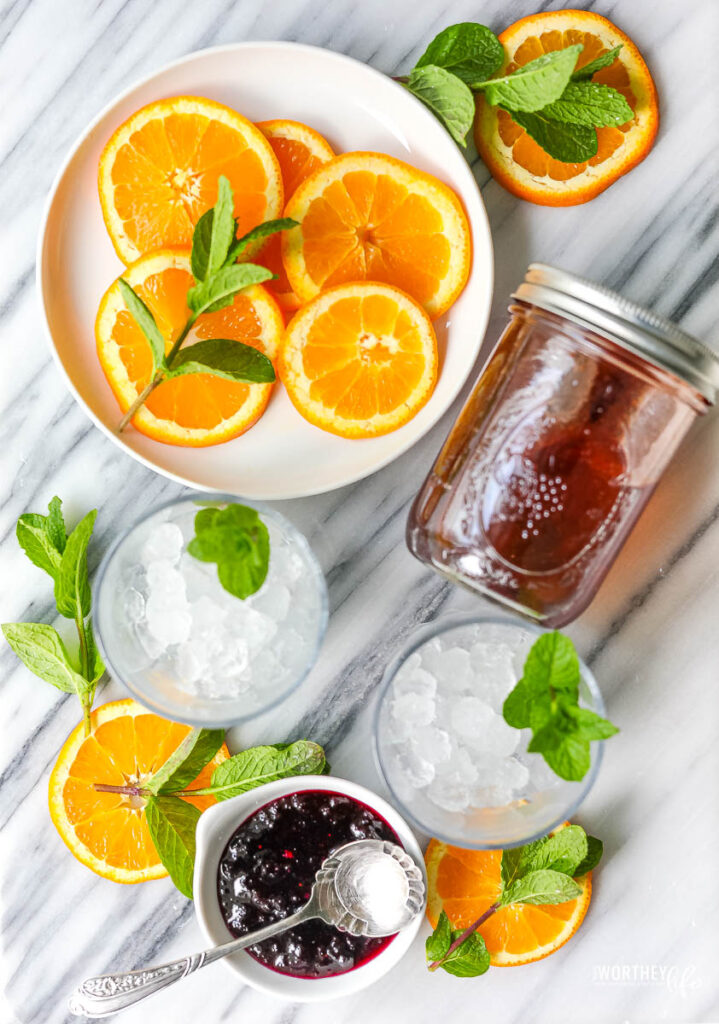 Blueberry Smash Syrup with orange slices on a white place and fresh mint leaves.