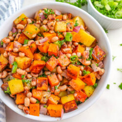 a white bowl filled with sweet potato and black eyed peas hash topped with parsley