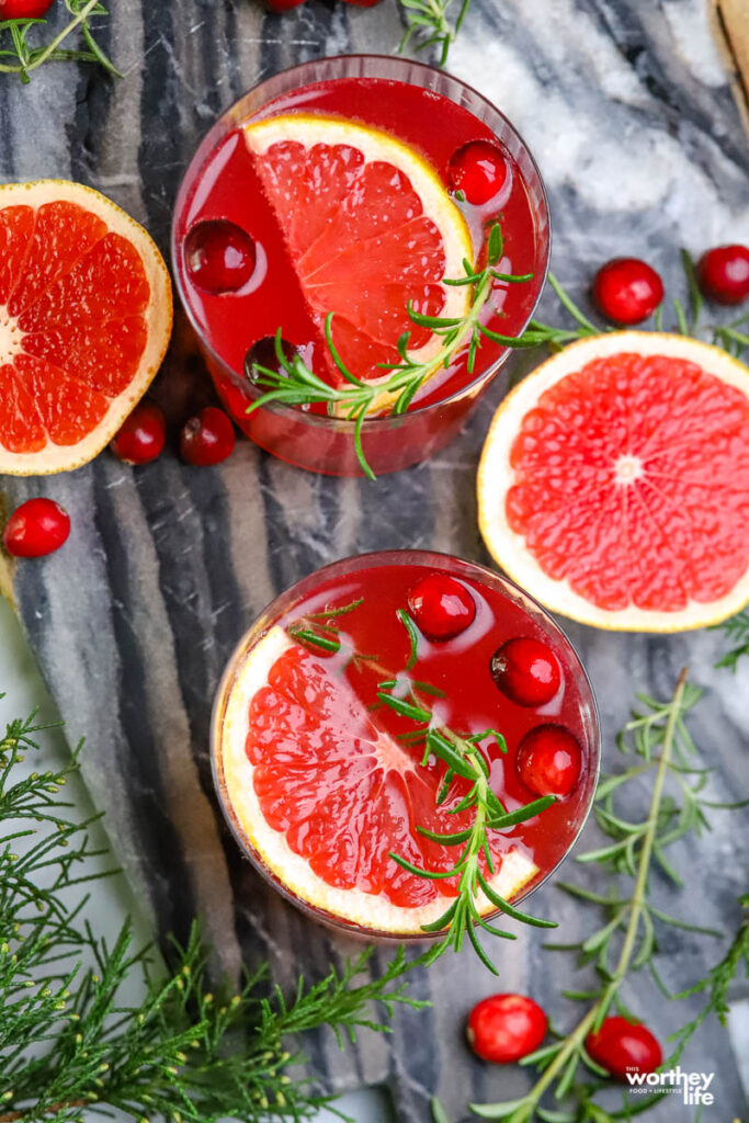 two cranberry cocktails with open grapefruit on cutting board