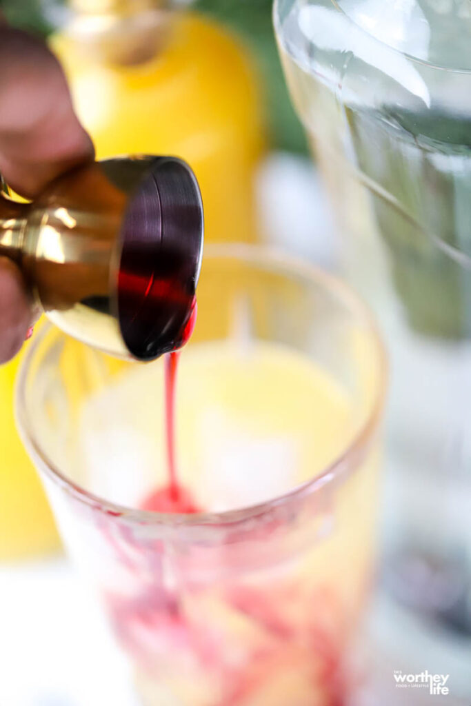 man's hand pouring red grenadine into a glass