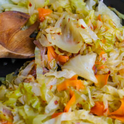 Fried cabbage in a skillet with a wood serving spoon