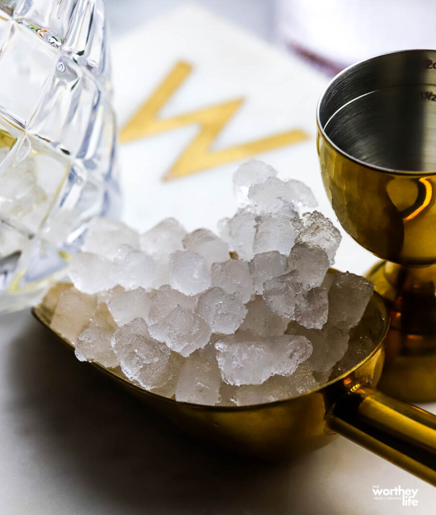 Pebbled ice in a gold ice scoop with a gold plated jigger.