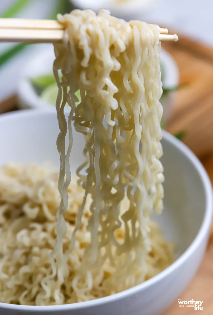 a white bowl of rice ramen with chopsticks.