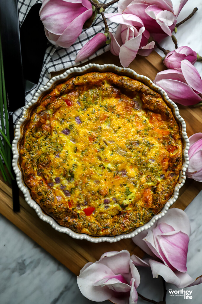 a delicious and easy salmon quiche in a pie pan on a wood board with flowers