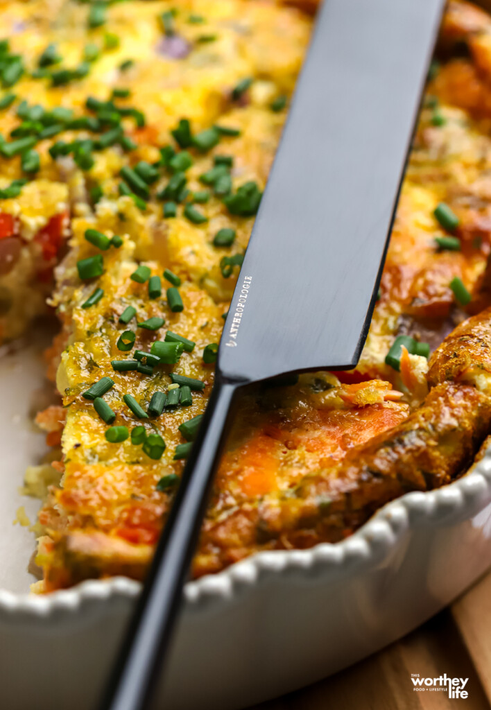 a black modern knife laying across a salmon crustless quiche