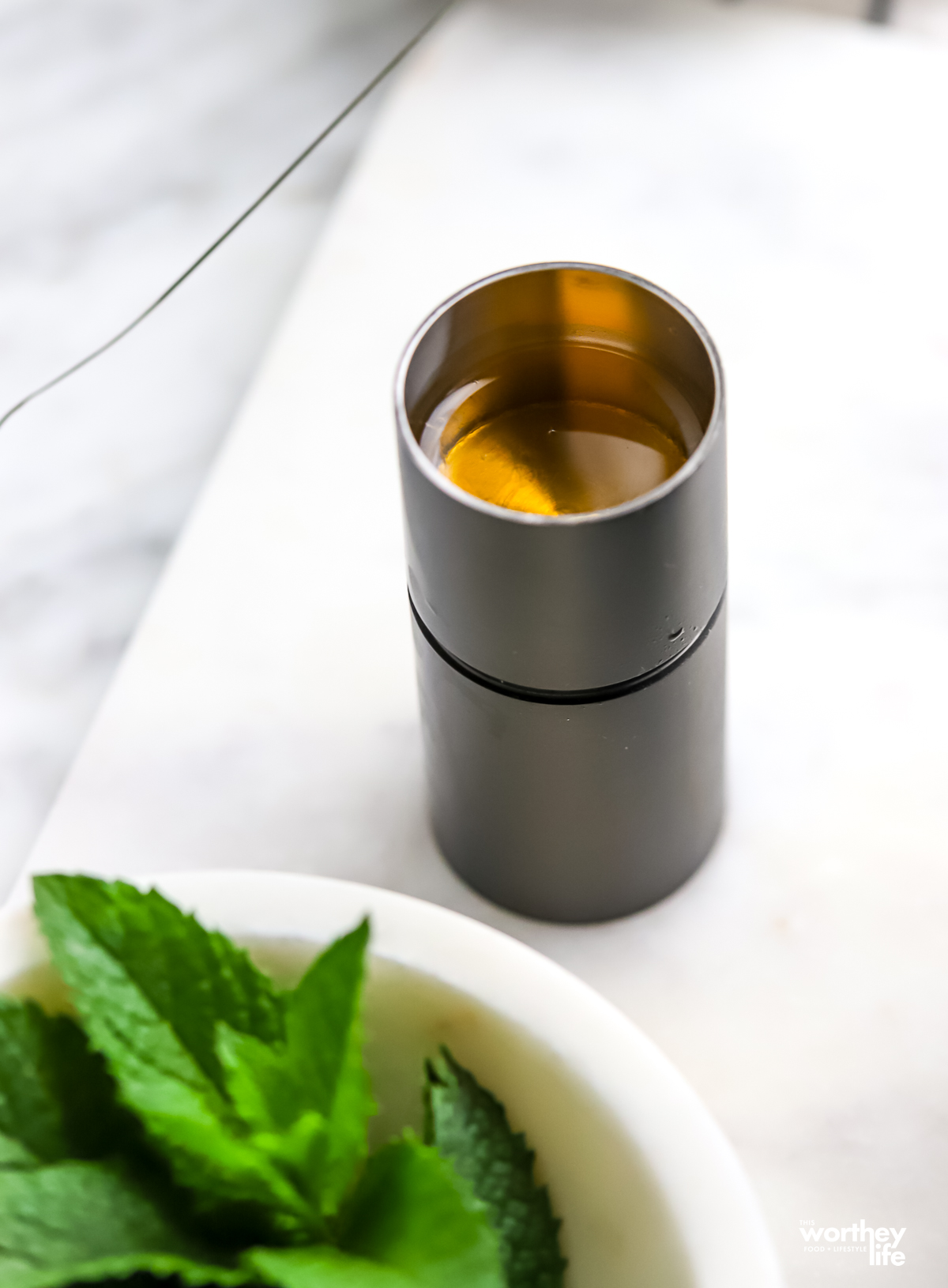 A cocktail jigger with organic blue agave and a partial view of a bowl filled with mint.