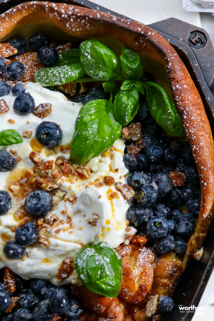 Blueberry Dutch Baby with toppings in a cast iron skillet.