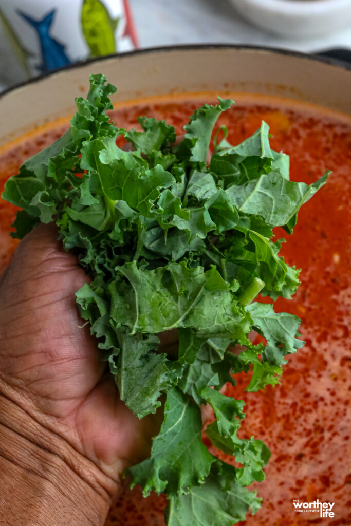 a man's hand holding fresh kale to put into a creamy tomato soup