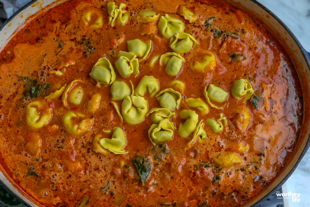 adding tortellini to a pot of tomato soup