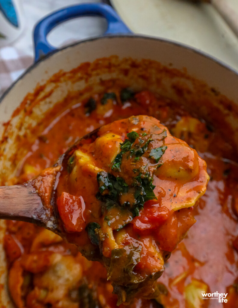 a ladle filled with creamy tortellini soup