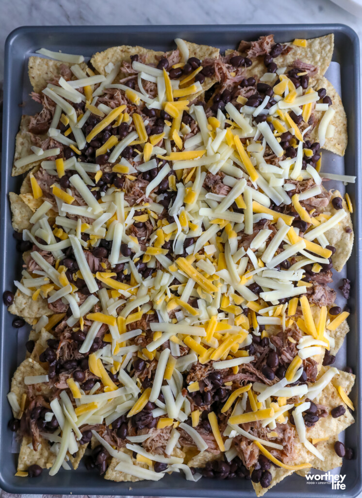 ingredients on tortilla chips ready to go to into the oven on a sheet pan