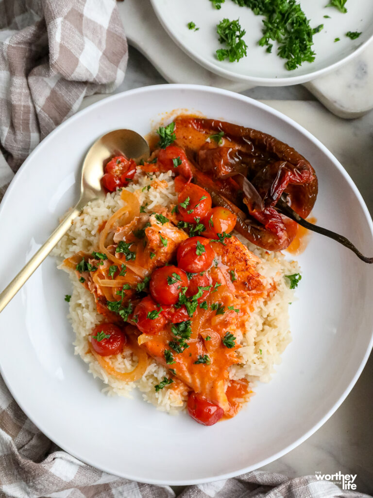 a plate of creamy tomato sauce with salmon over a bed of jasmine rice on a white plate