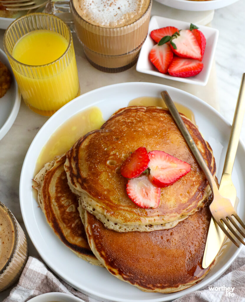 a stack of pancakes on a white plate with orange juice and coffee