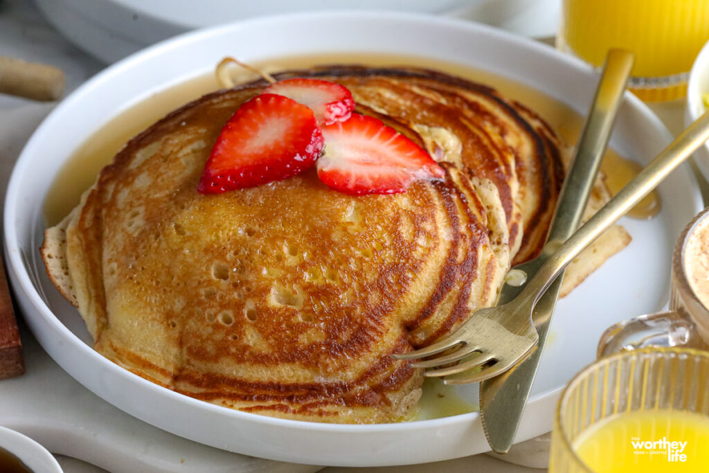 layers of homemade pancakes on a white plate with sugar and fresh fruit