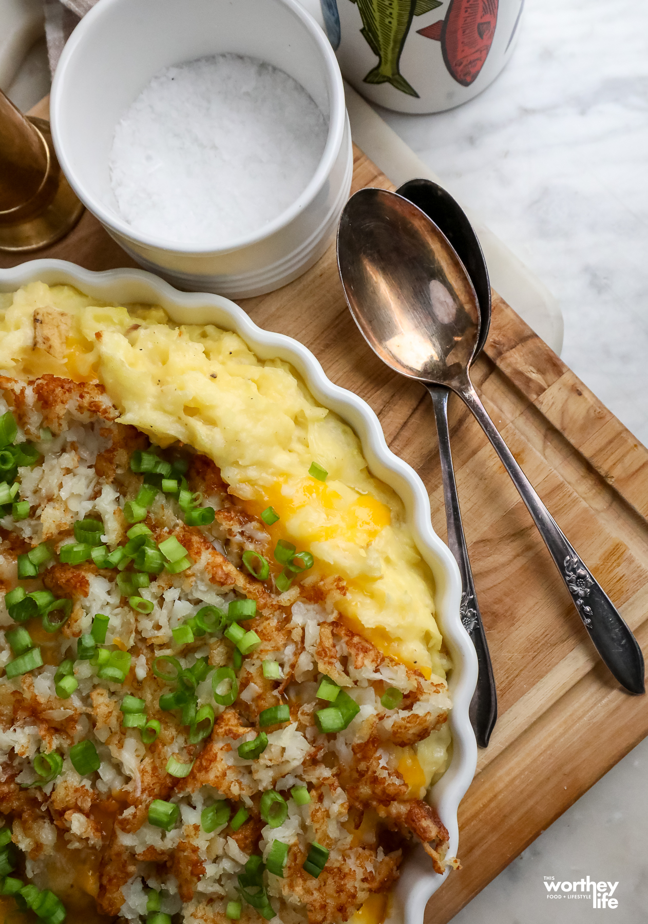 hashbrown mashed casserole in a white serving dish with spoons, salt